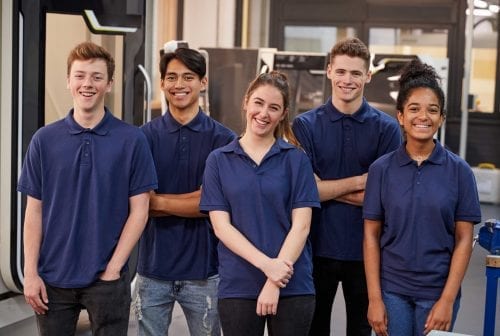 Five young apprentices in navy polo shirts standing together in a workshop
